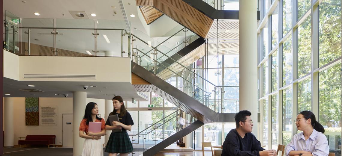 Four students in a foyer with an open stairwell in the background showing 2-3 levels.