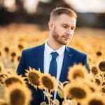 Luke Adams wearing a suit, standing in a field of sunflowers.