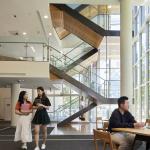 Four students in a foyer with an open stairwell in the background showing 2-3 levels.