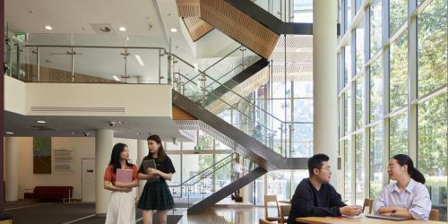 Four students in a foyer with an open stairwell in the background showing 2-3 levels.